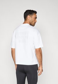 T-shirt branca de mangas curtas com um corte descontraído e um padrão subtil de texto impresso "RUNNING STATE OF MIND" nas costas.