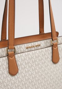 Sac cabas beige Michael Kors avec motif répétitif du logo MK et anses en cuir marron avec des détails métalliques dorés.