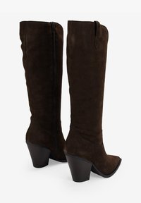 Botas altas de ante marrón, con punta afilada, tacón cuadrado y cierre de cremallera lateral. Presentan una textura suave y líneas de diseño limpias.