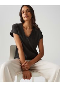 Top nero a V con maniche corte, tessuto testurizzato, vestibilità rilassata, abbinato a pantaloni a gamba larga di colore chiaro. Design semplice e moderno.