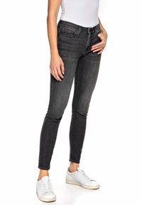 Jeans ajustados negros con cintura media, cinco bolsillos y costuras en contraste, combinados con zapatillas blancas y una camisa blanca entallada.