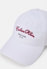 Cappello da baseball bianco in tessuto, con ricamo rosso del logo e del testo "Calvin Klein", dotato di visiera curvata e dettagli cuciti.