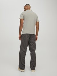Hellgraues Polohemd mit kontrastierendem Kragen und Ärmelbesatz, kombiniert mit dunkelgrauen weiten Hosen und beigen Sneakers.