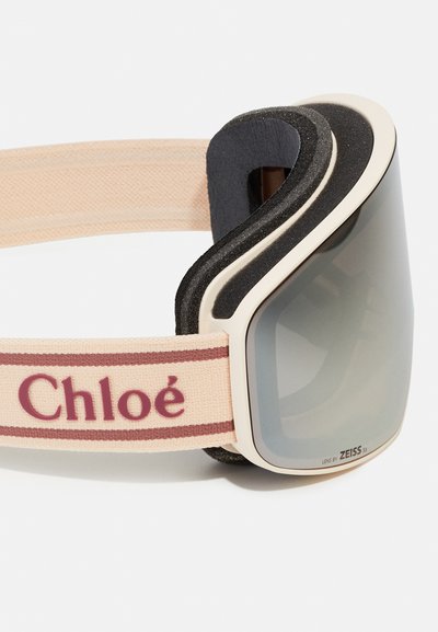 Ski brilles ar krēmveida rāmi, tumši pelēku lēcu un mīkstu melnu iekšpusi. Regulējamā siksna ir gaiši rozā ar bordo svītrām un "Chloé" tekstu.