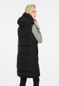 Schwarz gepolsterte Weste mit Kapuze, die ein elegantes Design, seitliche Taschen und einen strukturierten Stoff aufweist. Der Rücken ist glatt und hat auffällige Nähte.