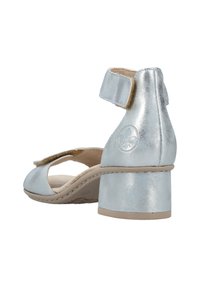 Silver metallic heeled sandal with a round toe, ankle strap, and cushioned footbed. Features a short block heel and decorative logo.