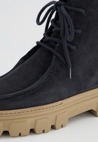 Botte en nubuck marine jusqu'à la cheville avec un bout rond, des lacets plats et une semelle en caoutchouc beige épaisse avec un motif de bande de roulement.