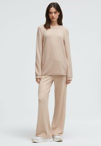 Beige Lounge-Set bestehend aus einem Langarm-Oberteil und einer weit geschnittenen Hose. Rippenstruktur und weicher Stoff. Kombiniert mit weißen Schuhen.