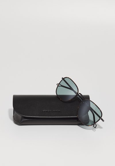 Ochelari de soare cu ramă de scoică și lentile verzi, așezați pe un elegant etui din piele neagră cu branding embossat.