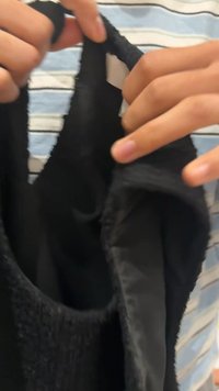 Top negro sin mangas hecho de tela texturizada, con un cuello ancho, forro suave y una etiqueta visible en el interior. Manos sosteniendo la prenda.