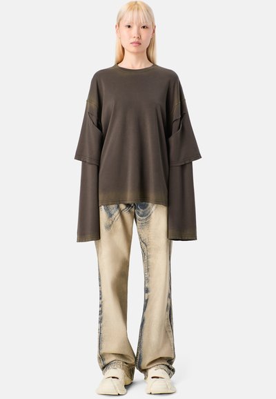 Overmaatse donkergroene katoenen t-shirt met brede mouwen, gecombineerd met lichtbeige denim jeans met een subtiele print, en crèmekleurige schoenen.