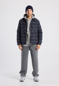 Blue checkered flannel jacket, gray hooded sweatshirt, gray baggy pants, and white sneakers. Model wears a navy beanie.