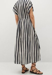 Maxikleid in Marineblau und Weiß mit gestreiftem Muster, kurzen Ärmeln und elastischem Bund, aus leichtem Stoff gefertigt; getragen mit schwarzen Sandalen mit Riemchen.