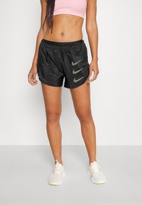 Černé sportovní šortky s lehkou, lesklou texturou, na levé straně se třemi šedými logy Nike a elastickým pasem.