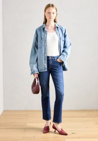 Denim särk valge topi peal, kombineeritud siniste teksade ja punaste laaditud nahast kõrgete kontsadega. Modell hoiab käes väikest tumepunast käekoti.