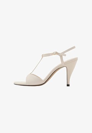 Sandalo T-strap beige con punta arrotondata, sottile cinturino alla caviglia e tacco di 7,5 cm. Finitura in pelle liscia e bordatura del sole nera a contrasto.