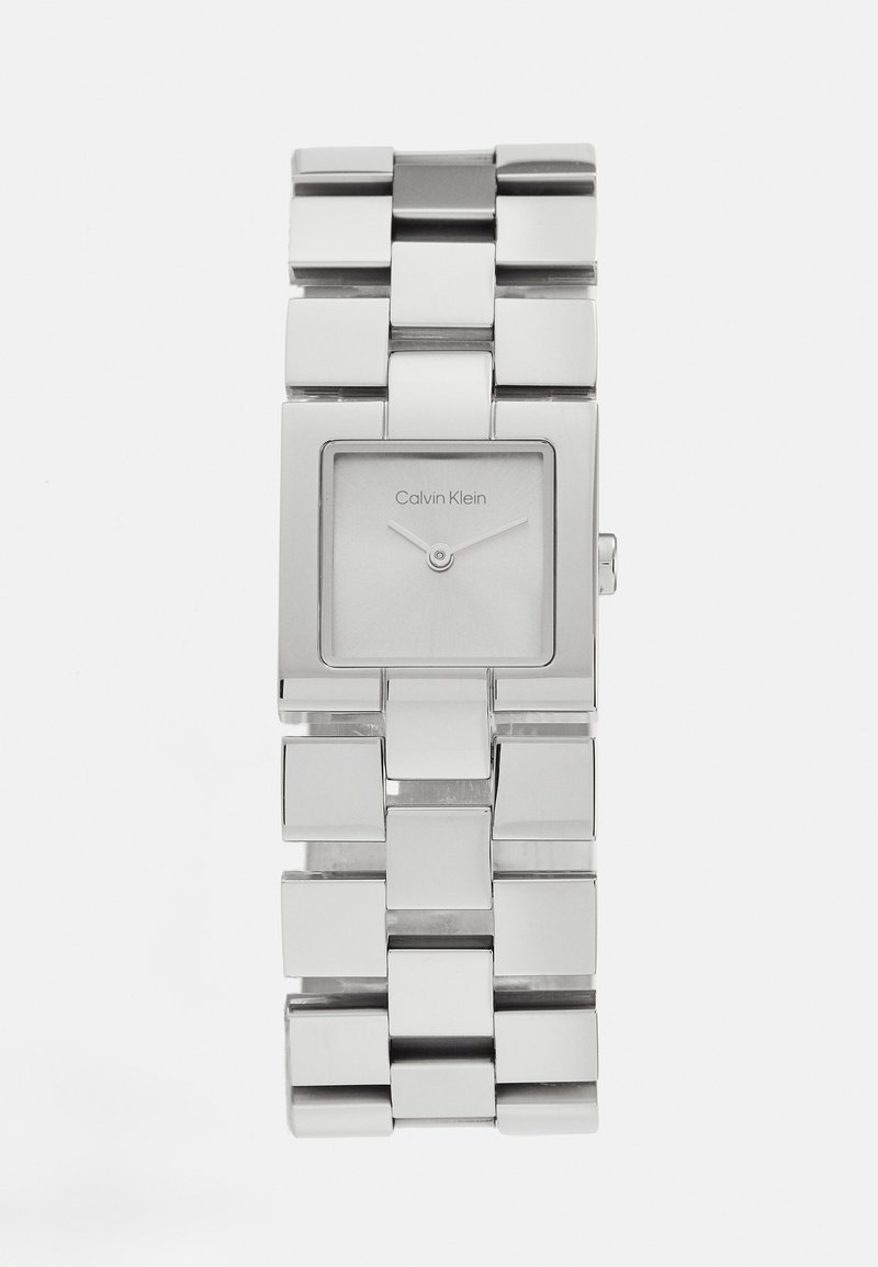 Montre en métal rectangulaire argentée avec un bracelet poli et un cadran minimaliste affichant des aiguilles des heures et des minutes, étiqueté "Calvin Klein".