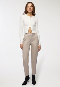 Dopasowany biały prążkowany top krótkie z rękawami z kołnierzykiem i zapięciem na zamek; w połączeniu z jasnobeżowymi spodniami o wysokim stanie i czarnymi botkami za kostkę.