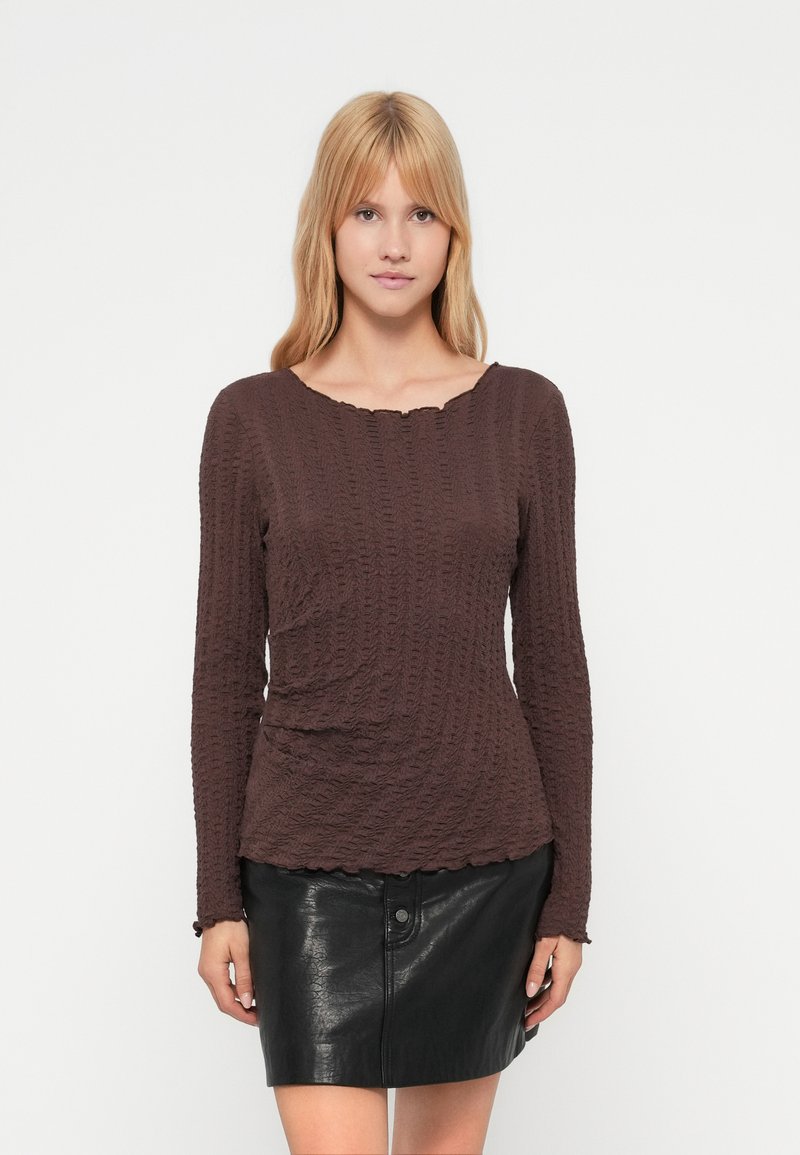 Καφέ τοπ με μακριά μανίκια και υφή με ριμπ σχέδιο. Διαθέτει λαιμόκοψη με κυματιστό περίγραμμα και φοριέται με μαύρη δερμάτινη μίνι φούστα.