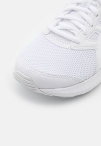 Chaussure de course blanche avec une tige en mesh, des lacets plats, un col rembourré et une semelle extérieure en caoutchouc épaisse. Texture lisse avec des détails de couture subtils.