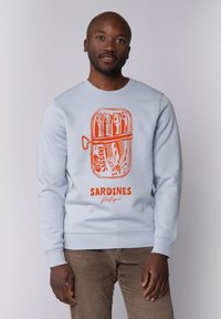 Sweatshirt bleu clair avec un graphique de boîte de sardines orange portant les inscriptions « SARDINES » et « Portugal », des poignets côtelés et une coupe décontractée.