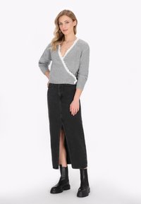 Maglione avvolgente grigio lavorato a maglia con bordo bianco a scallop, abbinato a una gonna di jeans nera con spacco alto e stivaletti neri con suola spessa.