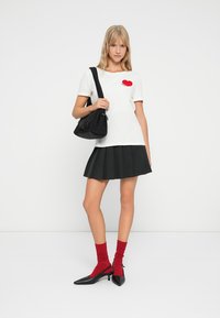 Λευκό κοντομάνικο μπλουζάκι με γραφικό κόκκινης καρδιάς, συνδυασμένο με μαύρη πλισέ φούστα, μαύρη τσάντα και κόκκινες κάλτσες μέχρι το γόνατο. Μαύρα ψηλοτάκουνα παπούτσια.