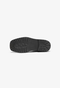 Suela de zapato de goma negra con un patrón de textura, que presenta estrías en ángulo y múltiples puntos de tracción para agarre y durabilidad.