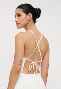 White backless dress with thin, crisscross straps and a tie closure at the lower back. Smooth fabric with a subtle sheen.