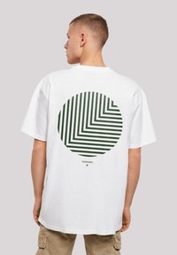 White cotton t-shirt featuring a large green circle design with alternating diagonal stripes. Relaxed fit with short sleeves and crew neck.