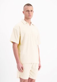 Lichtgele shirt met korte mouwen en bijpassende shorts met een textuurpatroon. Ontspannen pasvorm, knoopsluiting bij de kraag en detail van een borstzakje.