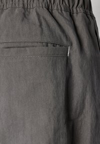 Gray pants made of textured fabric, featuring an elastic waistband and a single back pocket with visible stitching detail.