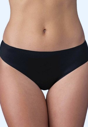 Zbliżenie na dolną część brzucha i biodra kobiety noszącej proste czarne majtki bikini na jasnym tle.