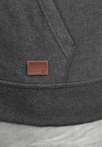 Gray sweatshirt with a ribbed hem, featuring a brown leather patch with "BLEND" logo and text. Soft texture and casual design details.