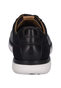 Černé kožené tenisky s hladkým povrchem, zaobleným podpatkem, bílou gumovou podrážkou a šněrováním v přední části s texturovanou poutkem na patě.