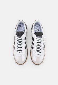 Vita sportskor med svarta ränder, rund tå, syntetiska och mocka material, strukturerade vita snören och märkta innersulor.