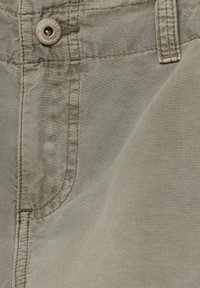 Pantalones de color caqui claro con una textura suave, costuras visibles y un botón de marca. El diseño incluye bolsillos laterales y un corte recto.