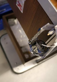 Silver wristwatch with a black face, metal case, and transparent strap. Features a visible brand label and an attached price tag.