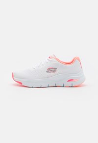 Zapatilla deportiva blanca con una parte superior de malla texturizada, detalles en rosa y una suela acolchada que presenta un soporte de arco visible.