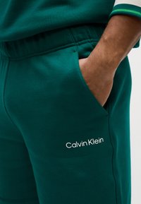 Mørkegrønne jogging shorts lavet af blødt materiale med en elastisk talje. Har en sidelomme og hvid "Calvin Klein" logo detalje.