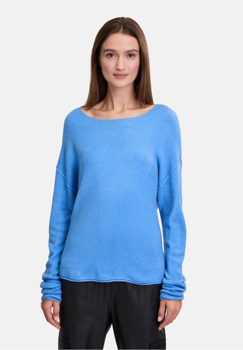 Pull bleu clair en matière douce, avec un col large, des manches longues à revers et une coupe décontractée. Associé à un pantalon noir.