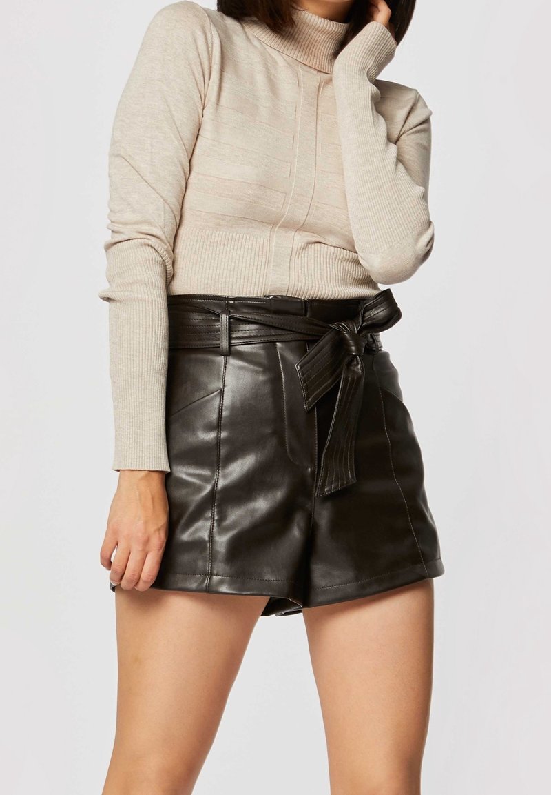 Mustat nahkahousut korkealla vyötäröllä ja vyöyksityiskohtana, yhdistettynä kermaiseen pitkähihaiseen ribbipäiseen turtleneck-neuleeseen.