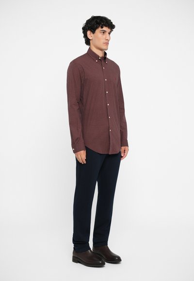 Cămașă lungă cu mâneci, cu un model roșu și marin, cu nasturi, asortată cu pantaloni marini și încălțăminte maro închis. Material neted cu o croială ajustată.