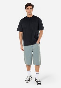 Black cotton t-shirt with short sleeves, paired with light blue denim shorts. Accessories include black and white sneakers and white socks.