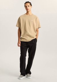 Beige lyhythihainen t-paita pyöreällä pääntiellä, yhdistetty mustiin rentoihin housuihin ja mustavalkoisiin ruudullisiin slip-on-kenkiin.