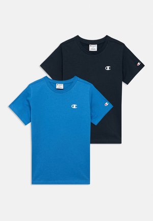 Δύο κοντομάνικα T-shirts της μάρκας Champion, ένα μπλε και ένα μαύρο, το καθένα με ένα μικρό λευκό λογότυπο στο στήθος και στο μανίκι.