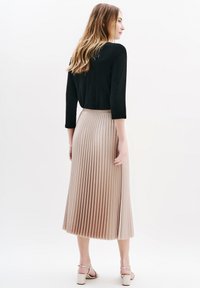 Schwarzes Oberteil mit drei Viertelärmeln, kombiniert mit einem knielangen, plissierten beigen Rock. Glatte Stofftextur mit klaren Faltenlinien und Seitenschlitz.