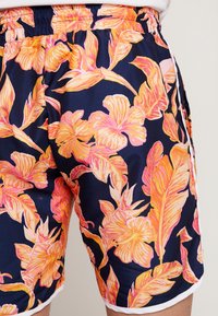 Shorts da bagno corti con vita elasticizzata. Realizzati in tessuto morbido, presentano uno sfondo blu navy vivace con ampi motivi floreali rosa e arancioni.