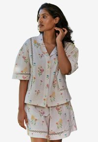 Light-colored floral short-sleeve pajama set in soft fabric. Features decorative lace accents and buttons on the front of the top.
