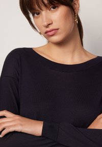 Granatowy sweter z dzianiny, z dekoltem łódką i długimi rękawami, o gładkiej fakturze i luźnym kroju. Subtelne detale szwów na ramionach.